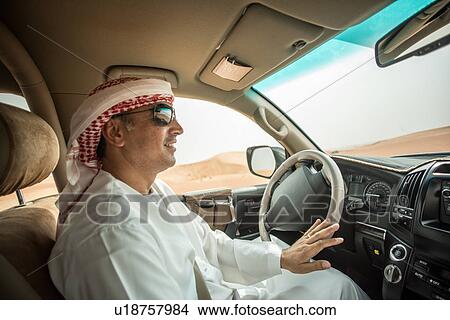 Picture - Middle eastern man wearing traditional clothes driving off road vehicle in desert, Dubai, United Arab Emirates. Fotosearch