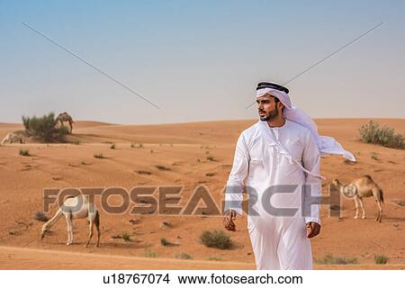 Middle eastern man wearing traditional clothes walking away from camels in desert, Dubai, United Arab Emirates View Large Photo Image Picture - Middle eastern man wearing traditional clothes walking away from camels in desert, Dubai, United Arab Emirates. Fotosearch