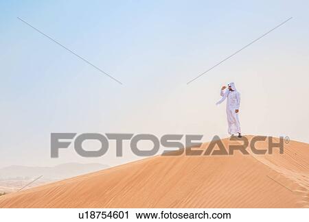 Middle eastern man wearing traditional clothes looking out from desert dune, Dubai, United Arab Emirates View Large Photo Image Stock Image - Middle eastern man wearing traditional clothes looking out from desert dune, Dubai, United Arab Emirates. Fotosearch