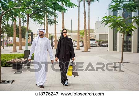 Middle eastern shopping couple wearing traditional clothing walking along street, Dubai, United Arab Emirates View Large Photo Image Stock Photo - Middle eastern shopping couple wearing traditional clothing walking along street, Dubai, United Arab Emirates. Fotosearch