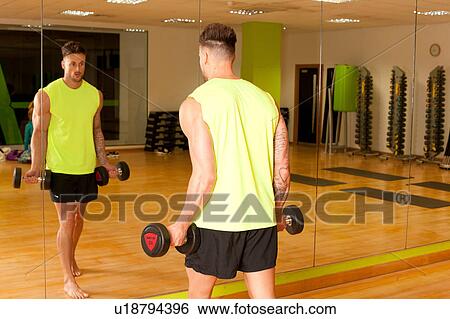 Stock Photograph - Mirror image of man at gym lifting dumbbells. Fotosearch