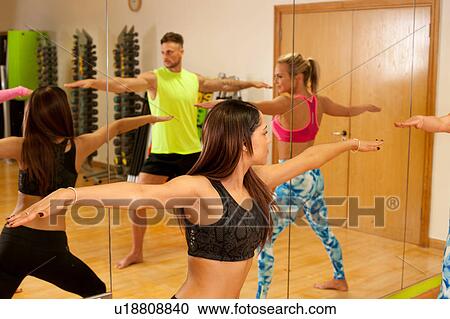 Stock Image - Mirror image of people in gym, arms open stretching. Fotosearch