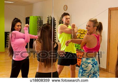 Stock Photo - Mirror image of people in gym doing arm stretching exercises. Fotosearch