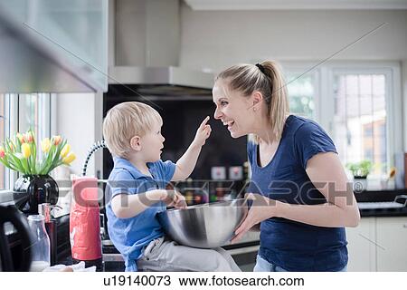 Stock Image - Mother and son fooling around whilst baking, son putting mixture on mother's nose. Fotosearch