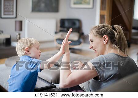 Stock Image - Mother and son giving high five, baby boy asleep on mother's lap. Fotosearch