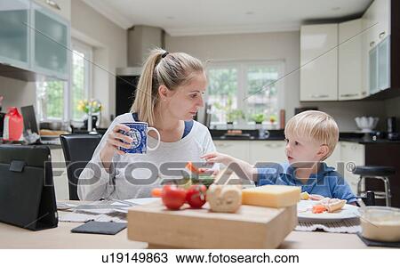 Stock Image - Mother and son sitting at table eating meal together. Fotosearch
