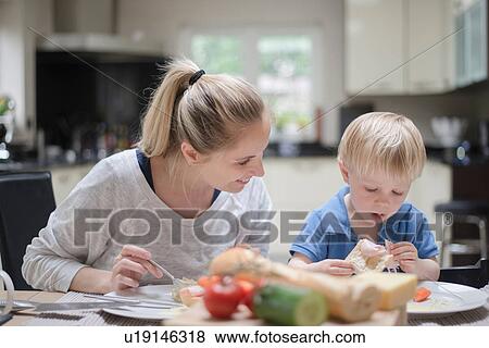 Stock Photo - Mother and son sitting at table eating meal together. Fotosearch