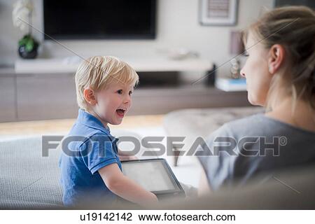 Mother and son sitting together, son holding digital tablet, laughing View Large Photo Image Stock Image - Mother and son sitting together, son holding digital tablet, laughing. Fotosearch