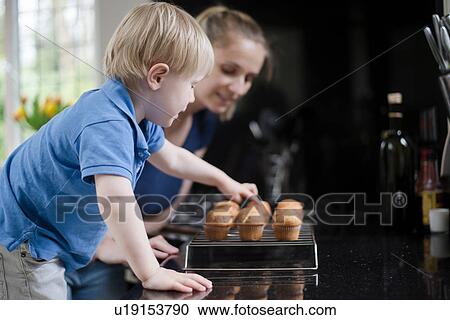 Stock Image - Mother and son waiting for freshly baked muffins to cool. Fotosearch