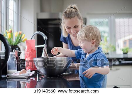 Stock Image - Mother helping son bake cake, son cracking egg. Fotosearch