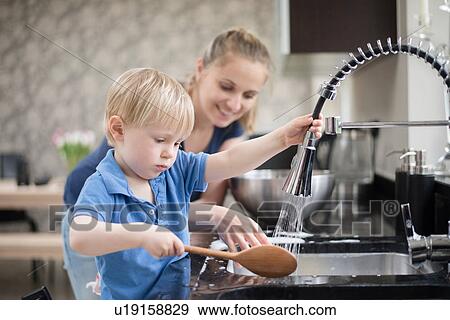 Stock Photo - Mother helping son wash wooden spoon. Fotosearch