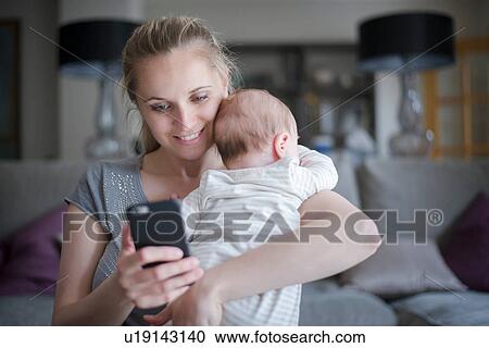 Mother holding baby boy whilst using smartphone View Large Photo Image Stock Image - Mother holding baby boy whilst using smartphone. Fotosearch