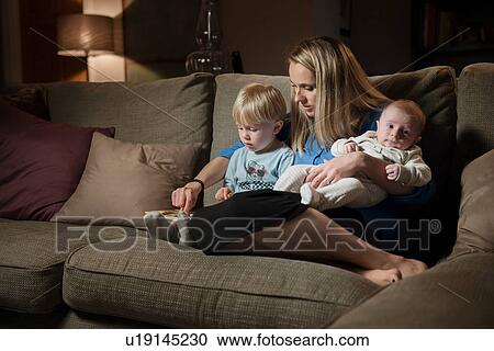 Stock Image - Mother relaxing on sofa with son and baby boy. Fotosearch