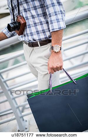 Neck down view of young man strolling on waterfront carrying shopping bag, Dubai, United Arab Emirates View Large Photo Image Stock Photo - Neck down view of young man strolling on waterfront carrying shopping bag, Dubai, United Arab Emirates. Fotosearch