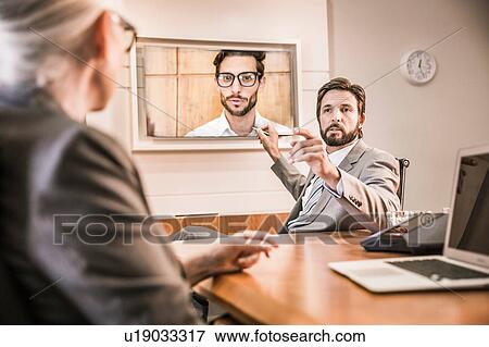 Over the shoulder view of business people in boardroom having video call meeting View Large Photo Image Stock Photo - Over the shoulder view of business people in boardroom having video call meeting. Fotosearch
