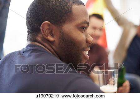 Over the shoulder view of man holding glass of beer looking away smiling View Large Photo Image Stock Photo - Over the shoulder view of man holding glass of beer looking away smiling. Fotosearch