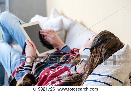 Over the shoulder view of woman wearing headphones using digital tablet View Large Photo Image Stock Photograph - Over the shoulder view of woman wearing headphones using digital tablet. Fotosearch