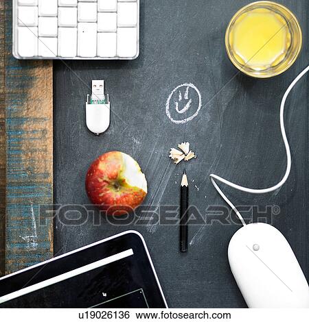 Stock Photograph - Overhead view computer equipment, apple and orange juice on blackboard surface. Fotosearch