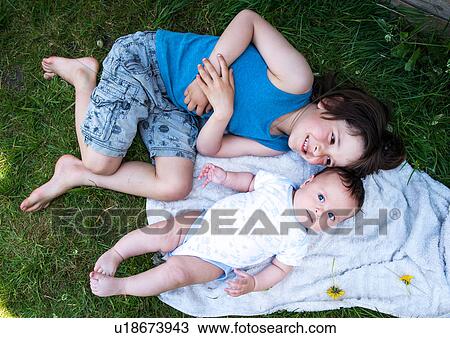 Stock Image - Overhead view of boy and baby brother lying in garden. Fotosearch