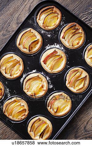 Stock Photo - Overhead view of miniature frangipane apple tarts in baking tray. Fotosearch