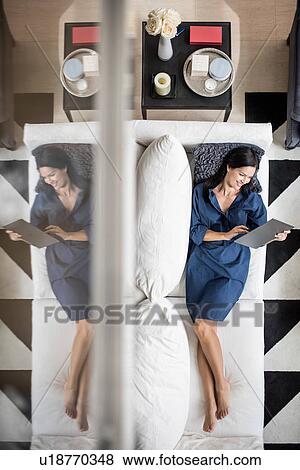 Stock Photo - Overhead view of woman lying on hotel room sofa using digital tablet, Dubai, United Arab Emirates. Fotosearch