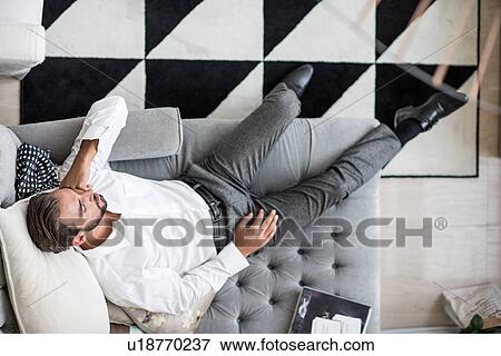 Overhead view of young businessman reclining asleep on hotel room chaise longue, Dubai, United Arab Emirates View Large Photo Image Stock Photo - Overhead view of young businessman reclining asleep on hotel room chaise longue, Dubai, United Arab Emirates. Fotosearch