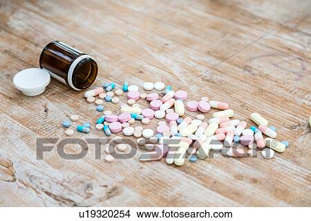 Picture - Pills and pill bottle on wooden surface. Fotosearch
