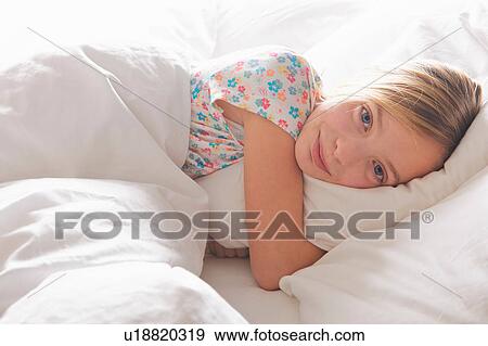 Stock Photo - Portrait of blond haired girl hugging pillow in bed. Fotosearch