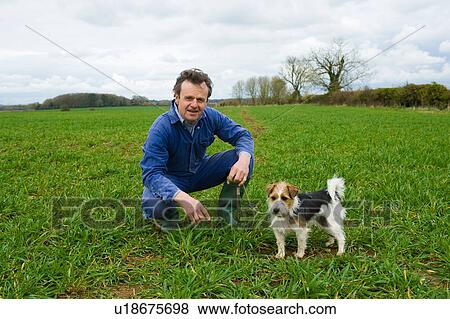 Stock Photo - Portrait of farmer crouching in field with dog. Fotosearch