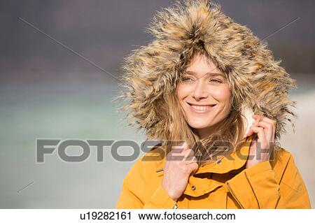 Stock Image - Portrait of mid adult woman outdoors, wearing fur trim coat, smiling. Fotosearch