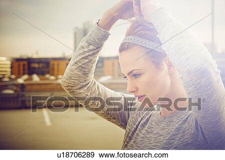 Stock Photo - Portrait of mid adult woman tying hair on rooftop parking lot. Fotosearch