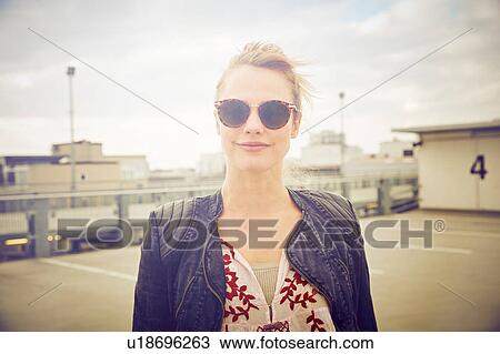 Stock Image - Portrait of mid adult woman wearing shades on rooftop parking lot. Fotosearch