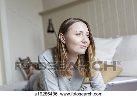 Portrait of woman lying on front on bed looking away smiling View Large Photo Image Stock Photograph - Portrait of woman lying on front on bed looking away smiling. Fotosearch