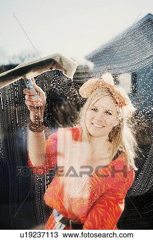 Stock Image - Portrait of woman outdoors cleaning window with squeegee. Fotosearch