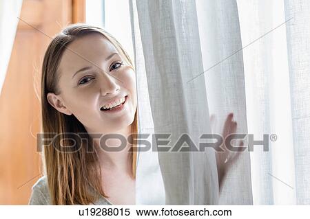 Portrait of woman peeking from behind curtain looking at camera smiling View Large Photo Image Stock Photography - Portrait of woman peeking from behind curtain looking at camera smiling. Fotosearch