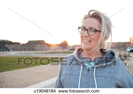 Picture - Portrait of woman wearing eyeglasses and hooded top looking away smiling. Fotosearch