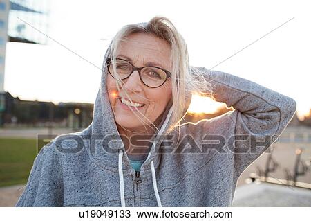 Stock Image - Portrait of woman wearing eyeglasses and hooded top looking at camera smiling. Fotosearch