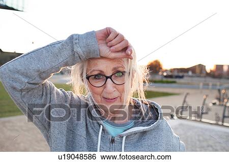 Portrait of woman wearing eyeglasses and hooded top, hand on forehead looking at camera smiling View Large Photo Image Stock Photograph - Portrait of woman wearing eyeglasses and hooded top, hand on forehead looking at camera smiling. Fotosearch