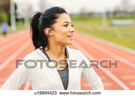 Stock Image - Portrait of young girl on running track, looking away, smiling. Fotosearch