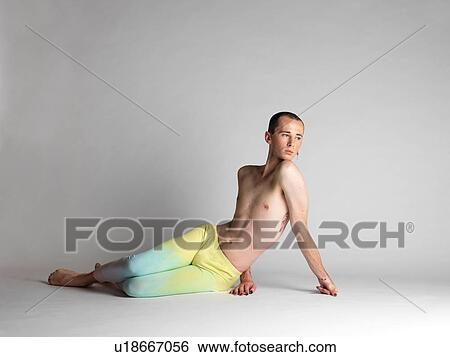 Stock Photograph - Portrait of young man wearing multi- coloured leggings sitting on studio floor looking away. Fotosearch