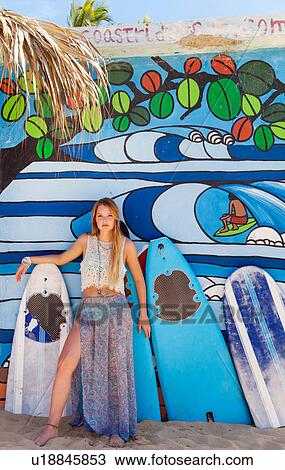 Stock Image - Portrait of young woman leaning against surfboard beach hut, Dominican Republic, The Caribbean. Fotosearch