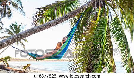 Stock Photograph - Portrait of young woman reclining in palm tree hammock beach, Dominican Republic, The Caribbean. Fotosearch