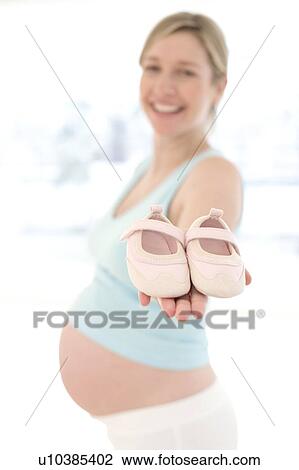 Stock Image - Pregnant woman holding baby shoes. Fotosearch