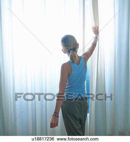 Stock Photograph - Rear view of girl peering through net curtained window. Fotosearch