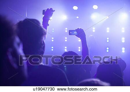 Rear view of group in club arms raised filming concert on smartphone View Large Photo Image Stock Image - Rear view of group in club arms raised filming concert on smartphone. Fotosearch
