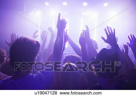 Stock Photo - Rear view of group in club arms raised watching concert. Fotosearch