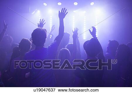 Stock Photo - Rear view of group in club arms raised watching concert. Fotosearch