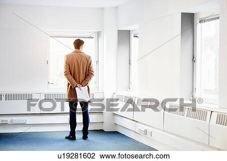 Rear view of man in empty office, hands behind back looking out of window View Large Photo Image Stock Image - Rear view of man in empty office, hands behind back looking out of window. Fotosearch