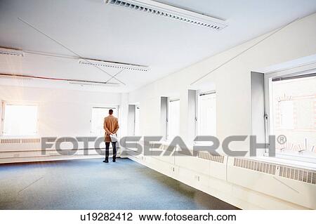 Rear view of man in empty office, hands behind back looking out of window View Large Photo Image Stock Image - Rear view of man in empty office, hands behind back looking out of window. Fotosearch