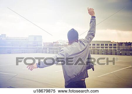 Stock Photography - Rear view of mid adult man dancing on rooftop parking lot. Fotosearch